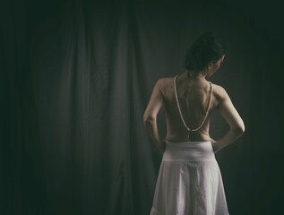 woman seen from behind with a white petticoat-type skirt and a pearl necklace in a romantic attitude
