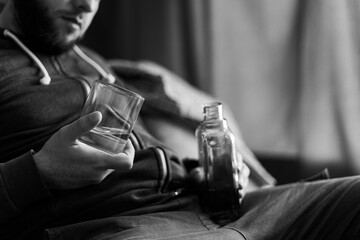 Drunk and lonely man holding whiskey bottle and glass sitting on sofa, close-up. alcohol addiction...