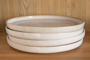 A stack of beige ceramic plates in a wooden cupboard.