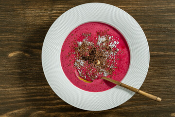 Sweet summer cherry soup in a white plate on a wooden background, closeup, top view. Hungarian cold red cherry soup with yogurt or cream, sprinkled with grated chocolate, powdered sugar and hazelnuts - 771431652