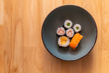 bowl of assorted sushi sits on a wooden table