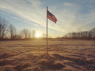 A lone American flag is standing in a field with a beautiful sunset in the background. The flag is the only thing in the scene, and it is the main focus of the image - obrazy, fototapety, plakaty