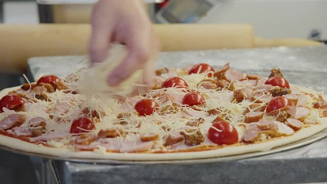 Preparing Italian pizza food by adding parmesan cheese ingredient. Preparing the delicious pizza with lots of melty cheese at the restaurant. Preparing the pizza by sprinkling the shredded cheese.