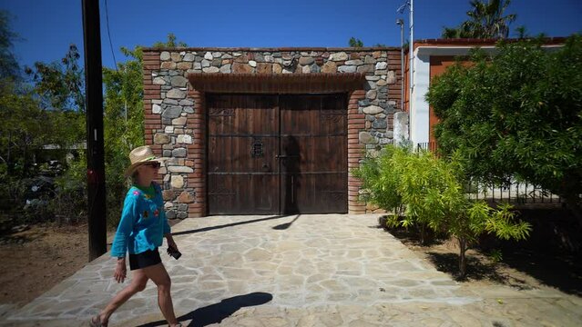 Female tourist wearing straw hat and ethnic, traditional clothes walking in front of home building in mining town of El Triunfo, Mexico.