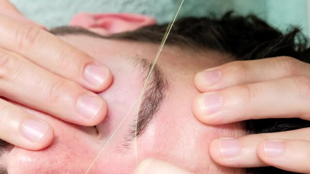 Horizontal 4K close up video of a male eyebrow waxing with threading on a young woman in a beauty salon. Concept of wellness and body care