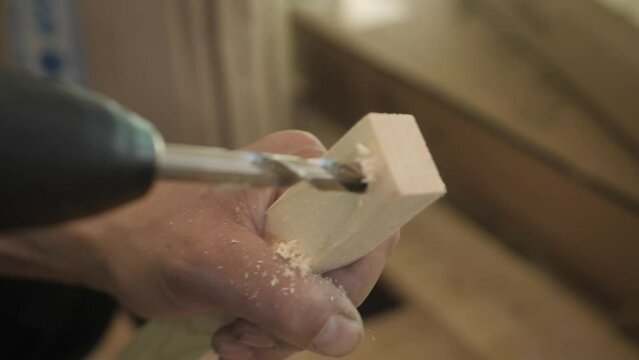 Close-up of drilling into wood with twisted screw, metal drill bit making holes in a wooden oak plank. Man carpenter hand boring holes.