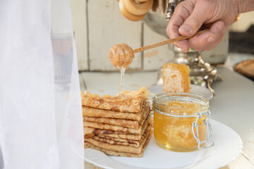 A man pours honey on pancakes and drinks tea from a samovar, Russian tradition of celebrating Maslenitsa