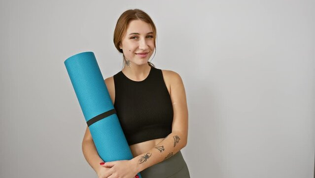 Ebullient young brunette girl in sportwear, confidently flashing a toothy grin as she holds her yoga mat, over isolated white background.