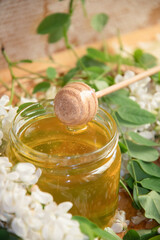 still life of a full jar of transparent yellow ocacia honey on the table against the background of wax honeycombs