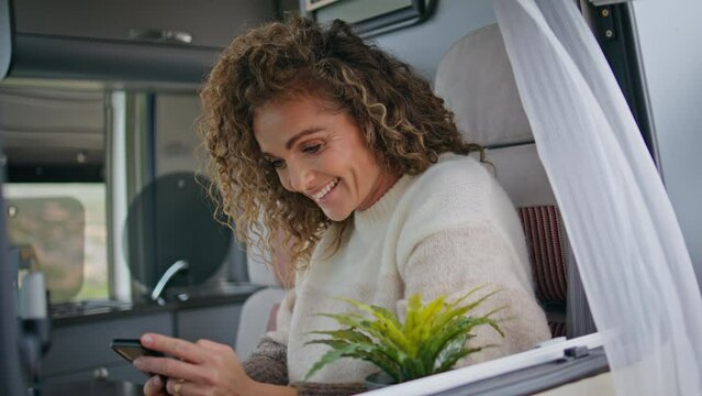 Cheerful lady reading message cellphone sitting motorhome window close up. 