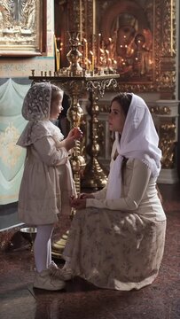 a mother and daughter in a temple or church hold a candle and pray, sad relatives people put candles, introducing children to the sacraments of the church