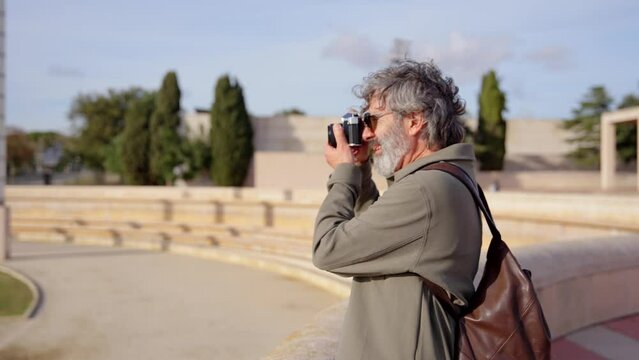Senior tourist man taking a photo on retro camera. Photographer exploring the park.