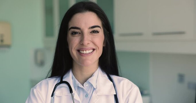 Close up head shot of millennial enthusiastic Latina general practitioner, looks competent and reliable posing alone in medical office. Health-care worker portrait, mission and professional occupation