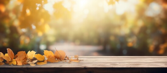 A wooden table adorned with vibrant autumn leaves sits against a blurry background, creating a natural landscape with tints and shades of orange and brown - obrazy, fototapety, plakaty
