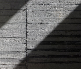 Detalle de muro de hormigón parcialmente iluminado con luz solar rasante que resalta la textura de...