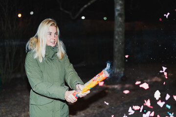A young girl shoots confetti from a firecracker on the street on a holiday at night.