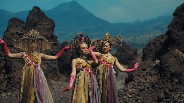Traditional dancers in ornate costumes performing in a volcanic landscape with mountains in the background.