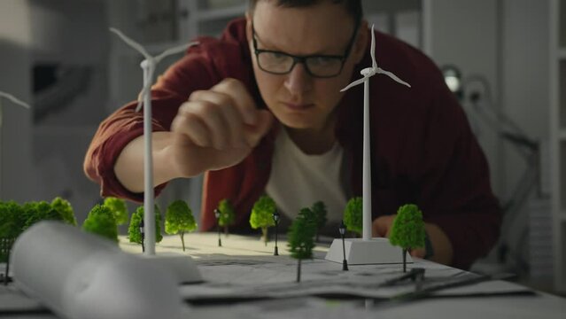 A young white male design engineer is working on the implementation of windmills in a modern office. Its goal is to develop innovative concepts for future cities based on green energy