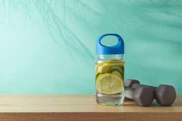 Summer fitness background with infused water bottle and dumbbells on wooden table over blue...