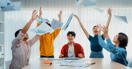 Excited and happy startup company employee celebrate and throw paper in the air after make...