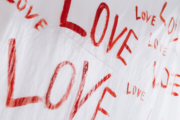 Multiple drawings of the word LOVE hand-painted in bright red forming a pattern on a plain white surface oilcloth, Valentine`s day concept celebration decoration in photo studio. Love, holiday, party
