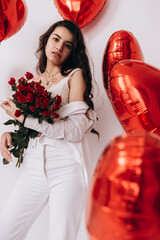 A smiling woman with kisses lipstick is holding a bouquet of red roses and standing amidst heart-shaped helium balloons, possibly celebrating a special occasion like Valentines Day

