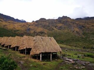 many thatched houses in the field with mountains behind them