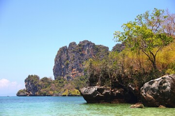 Obraz premium Tranquil sea with a rocky shoreline and lush vegetation. Railay Beach, Thailand.