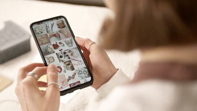A young woman is looking through a photo gallery using a smartphone. A girl looks at images on social networks on her phone screen.