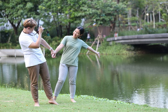 man couple holds a camera to take photos of his Asian female friend and takes pictures of the scenery while walking and relaxing in the garden. The couple walks barefoot on the grass in the garden.