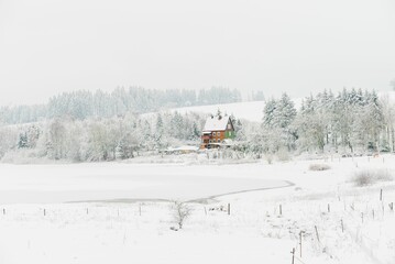 a rural scene with some trees and an old house on the bank of a frozen