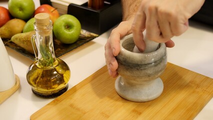 A man's hand grinds pepper in mortar and pestle crushing spices for seasoning With skillful motions he grinds spices releasing their aroma The spices are meticulously ground, intensifying their flavor