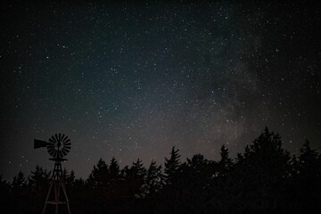 Astrophotography of the night sky taken over a single windmill in the rolling sandhills of Nebraska