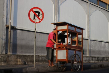 a meatball vendor (tukang bakso) sells under a no-parking notice board