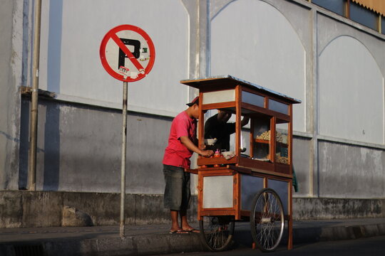 a meatball vendor (tukang bakso) sells under a no-parking notice board