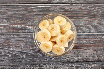sliced banana bowl on wood background top view