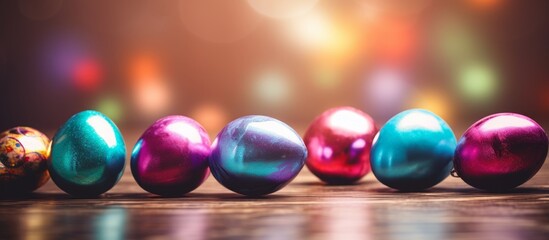 A creative arts display featuring a row of colorful Easter eggs made of glass and natural materials, including shades of purple, pink, magenta, and violet, resting on a wooden table