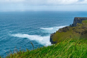 Lush, green grassy field with gentle waves lapping against the cliffson a cloudy day