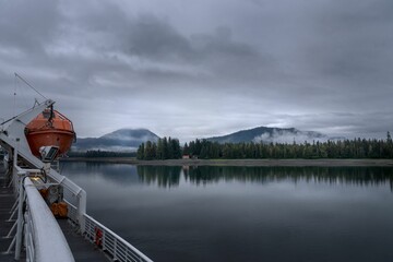 a boat docked on the shore near a mountain range on a cloudy day - Powered by Adobe