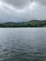 Tranquil lake against a backdrop of majestic mountains, with a cloudy sky and dark clouds overhead