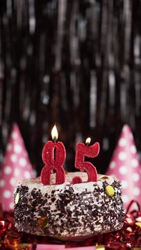 Number eighty-five birthday candle on sweet cake on dark background, 85th birthday. Blow out the holiday candle.