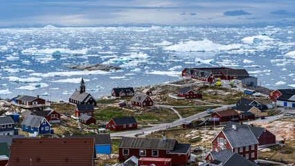 Blick auf die bunten Häuser von Ilulissat mit den treibenden Eisschollen der Diskobucht im...