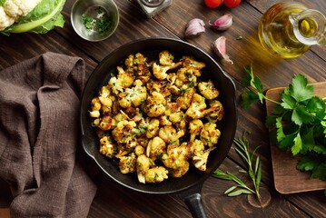 Roasted cauliflower in cast iron pan on wooden table. Top view, flat lay