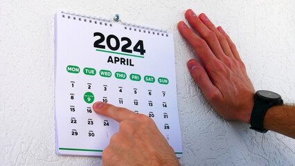 Close-up of a male hands pointing finger at the Eid al-Fitr date on the April page of a wall...