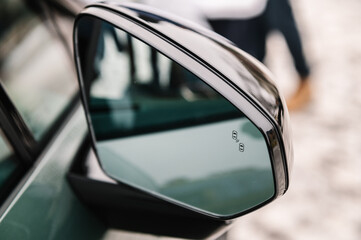 Blind zone monitoring sensor on the side right mirror of a new modern electric sedan car. View of...
