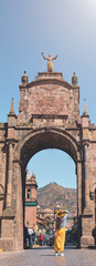 Obraz premium Young woman traveler in brown hat walks through of the Santa Clara Arch in San Francisco square. Cusco, Peru.