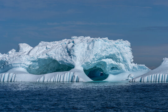 Eisberg treibt in der Diskobucht bei Ilulissat, durch den Sonnenschein sieht man die türkise Farbei im Wasser, Teile sind bereits geschmolzen oder abgebrochen und der Eisberg hat Löcher