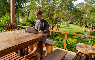 Young man telecommuting with his laptop on the terrace of his house outdoors, spring garden.