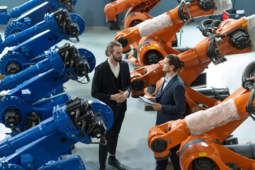Two professionals in suits engaged in a discussion amid advanced industrial robots in a technology...