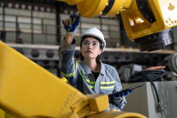 Female industrial engineer in hard hat inspecting new robot arms machinery components while holding...